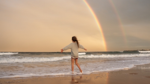 Anonymous woman on beach with rainbow