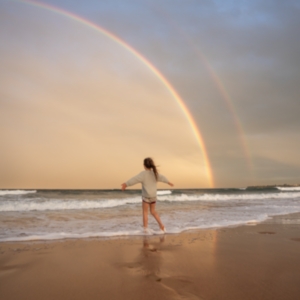 Anonymous woman on beach with rainbow