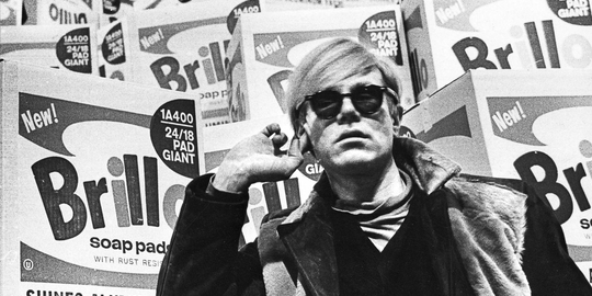 Image of Andy Warhol in front of Brillo boxes
